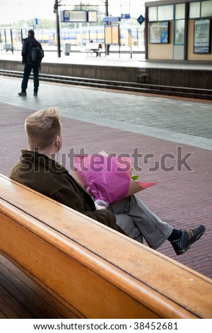 man on a railway-station with flowers waiting for
