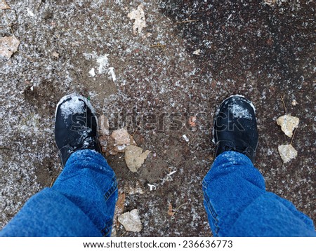 Feet on the asphalt with dry leaves and first snow.