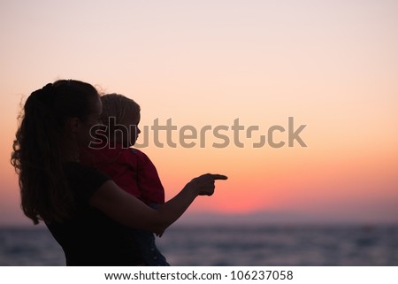 Silhouette of mother with baby in sunset pointing on copy space