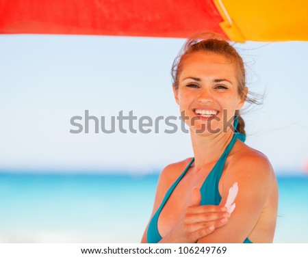 Happy woman applying sun block creme on arm