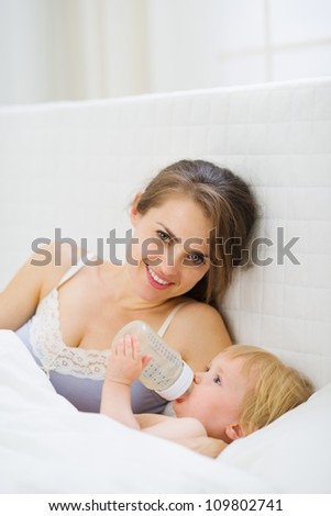Mother laying near drinking water baby in bed