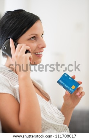 Happy young woman with credit card speaking mobile