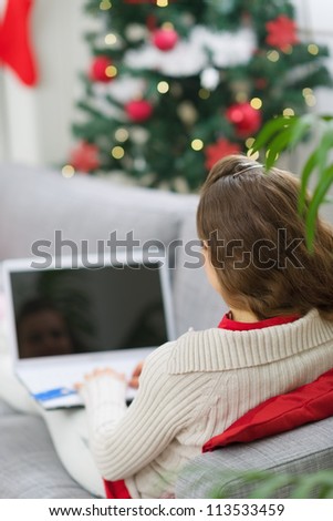 Woman using laptop near Christmas tree. Rear view