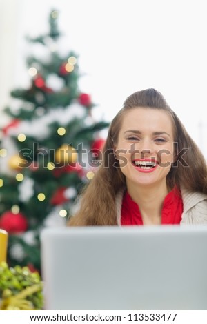 Happy young woman near Christmas tree with laptop