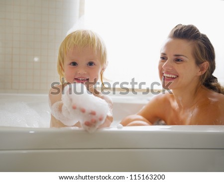 Baby playing with foam while taking bath with mother
