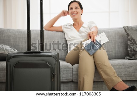 Dreaming woman with passport and air ticket sitting on couch
