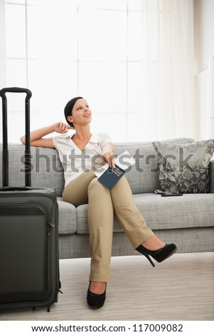 Dreaming woman with passport and air ticket sitting on sofa