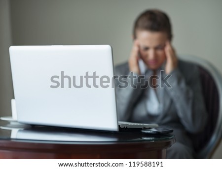 Closeup on desk with phone and laptop and stressed business woman in background