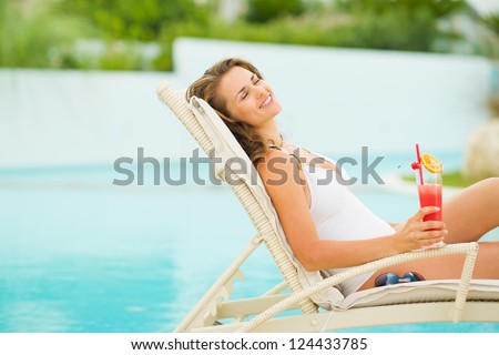 Young woman in swimsuit relaxing with cocktail on chaise-longue