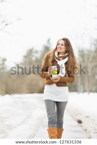 Happy young woman with hot beverage walking in winter park