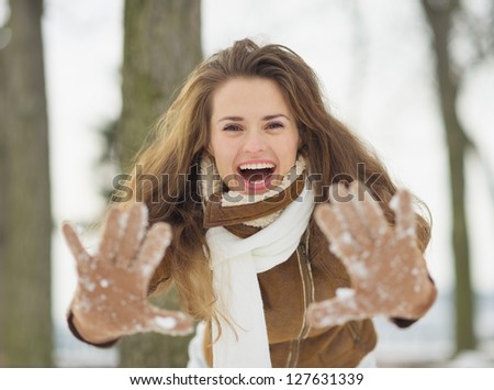 Happy young woman showing hands in snowed gloves in winter park