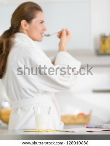 Closeup on glass of milk and magazine on table and young woman in bathrobe in background