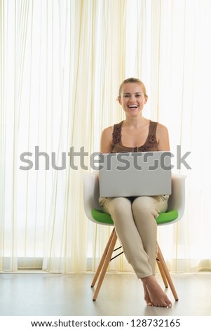 Happy young woman sitting on modern chair with laptop
