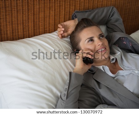 Business woman talking cell phone on bed in hotel room