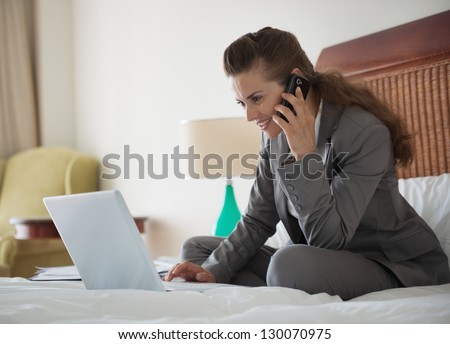 Business woman talking mobile phone and working on laptop in hotel room