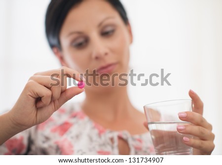 Closeup on pill and glass of water in hand of concerned young woman