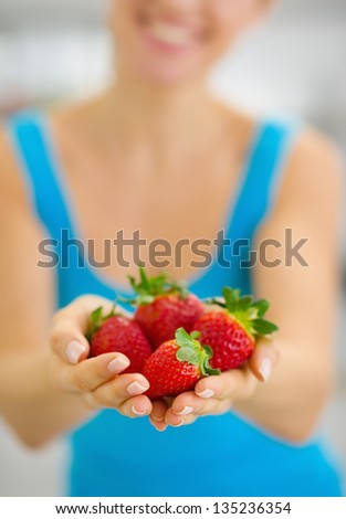 Closeup on smiling young woman giving strawberries