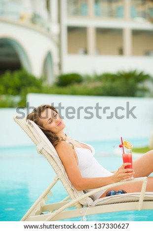 Happy young woman with cocktail enjoying laying on chaise-longue
