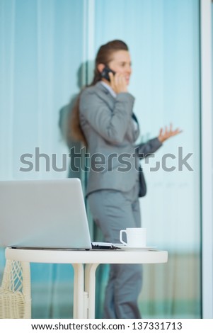 Closeup on table with laptop and cup on terrace and talking mobile phone business woman in background