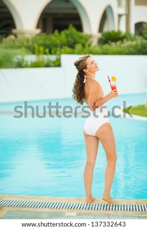 Full length portrait of young woman relaxing with cocktail at poolside