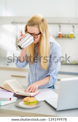 Young woman drinking coffee while studying in kitchen