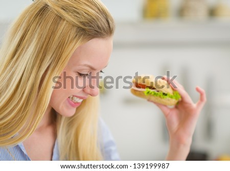Happy young woman eating sandwich in kitchen