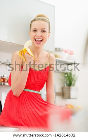 Happy young woman eating banana in kitchen