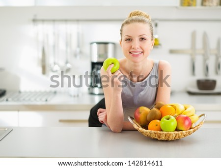 Happy Young Housewife With Apple In Modern Kitchen