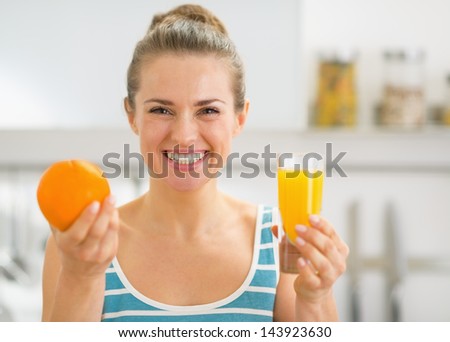 Smiling young woman showing glass of orange juice and orange