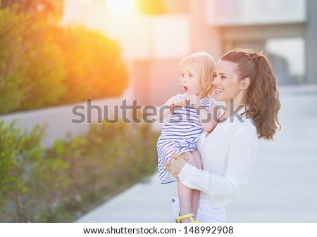 Happy mother and baby in front of house building looking on copy space