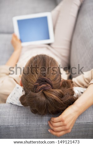 Young woman laying on sofa with tablet pc . rear view