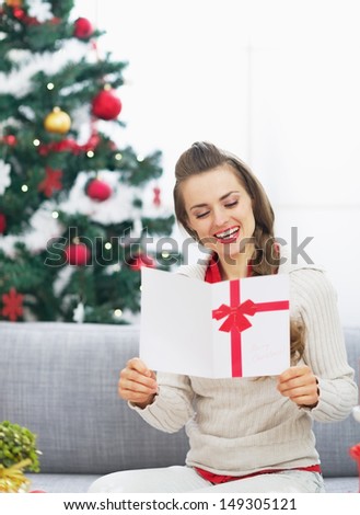 Happy young woman reading christmas postcard near christmas tree