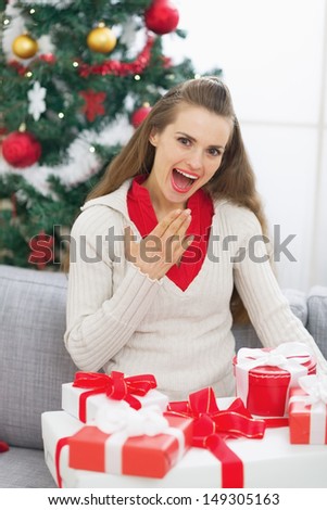 Surprised young woman with christmas present boxes near christmas tree