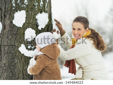 Happy mother and baby making face for tree using snow