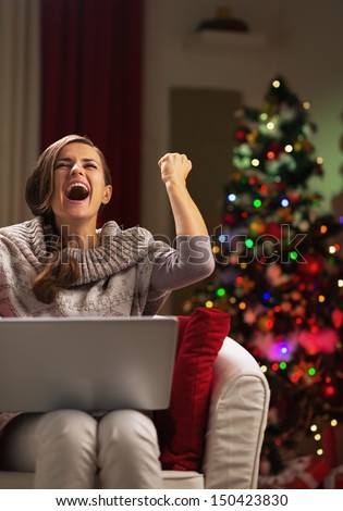 Happy young woman with laptop near christmas tree rejoicing