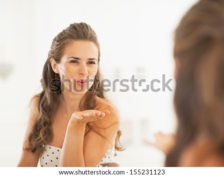 Young woman blowing air kiss in mirror