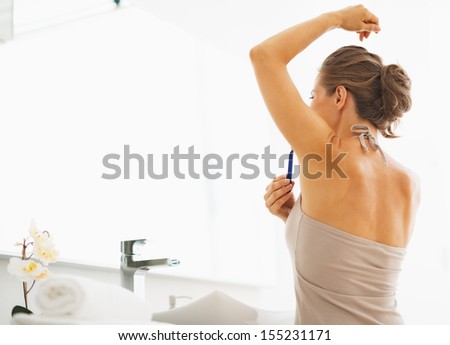 Woman shaving armpit in bathroom