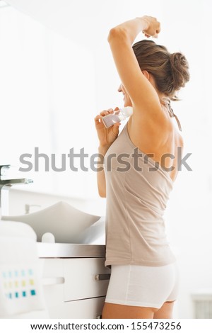 Woman applying roller deodorant on underarm in bathroom