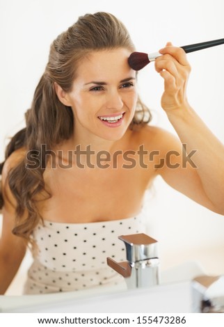 Happy woman using makeup brush in bathroom