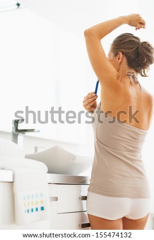 Woman shaving armpit in bathroom