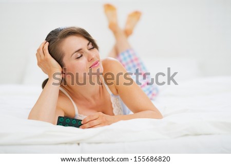 Happy young woman laying in bed with blister package of pills