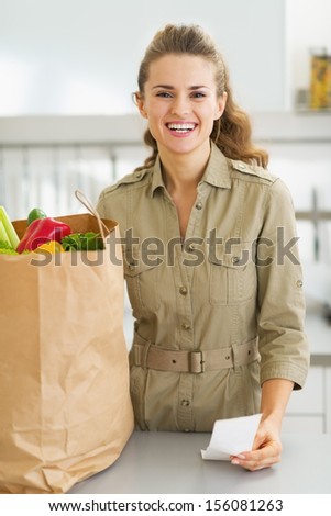 Happy young housewife with check and shopping bag full of vegetables