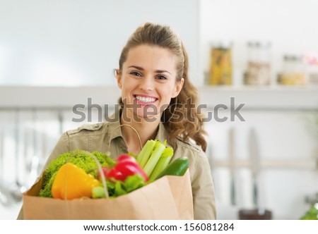 Happy young housewife with shopping bag full of vegetables