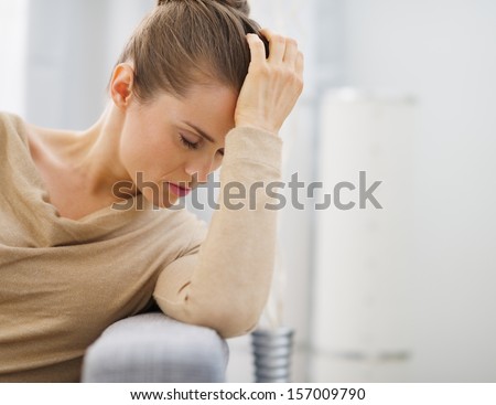 Portrait of stressed young housewife sitting on divan