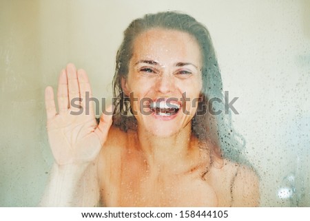 Smiling young woman looking through weeping glass in shower