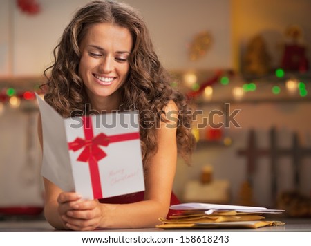 Happy young housewife reading christmas postcard in kitchen