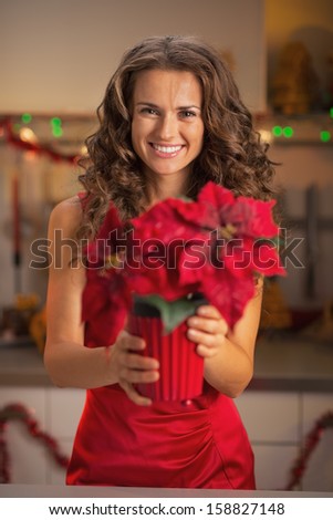 Happy young woman in red dress holding christmas rose in christmas decorated kitchen