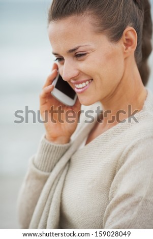 Happy young woman in sweater on beach talking cell phone