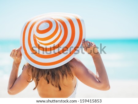 Young woman in swimsuit beach hat looking into distance . rear view