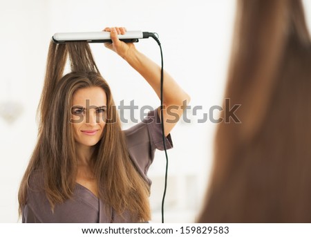 Portrait of woman straightening hair with straightener